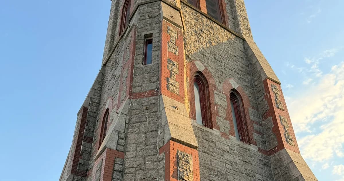 Granite and red-brick church tower against a blue sky in Fall River