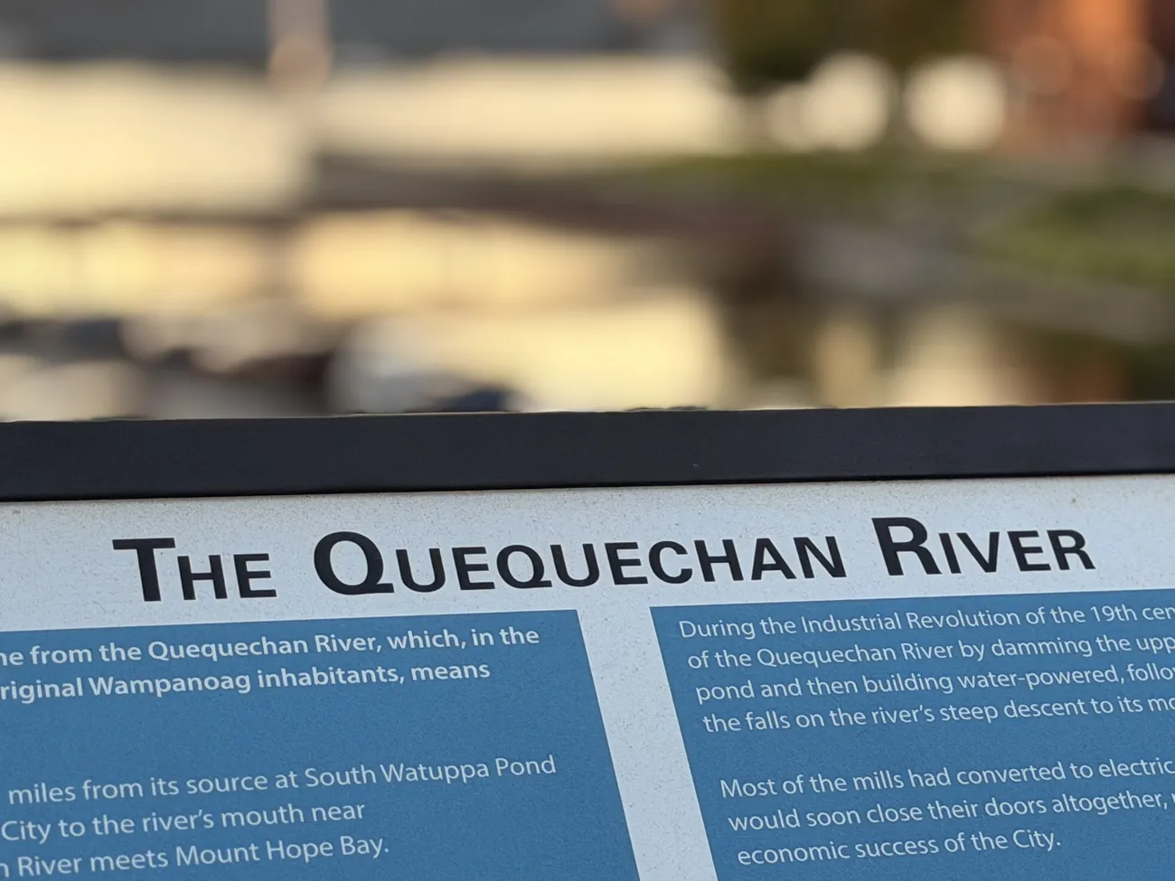 The Quequechan River interpretive sign, with the battleship beyond it.