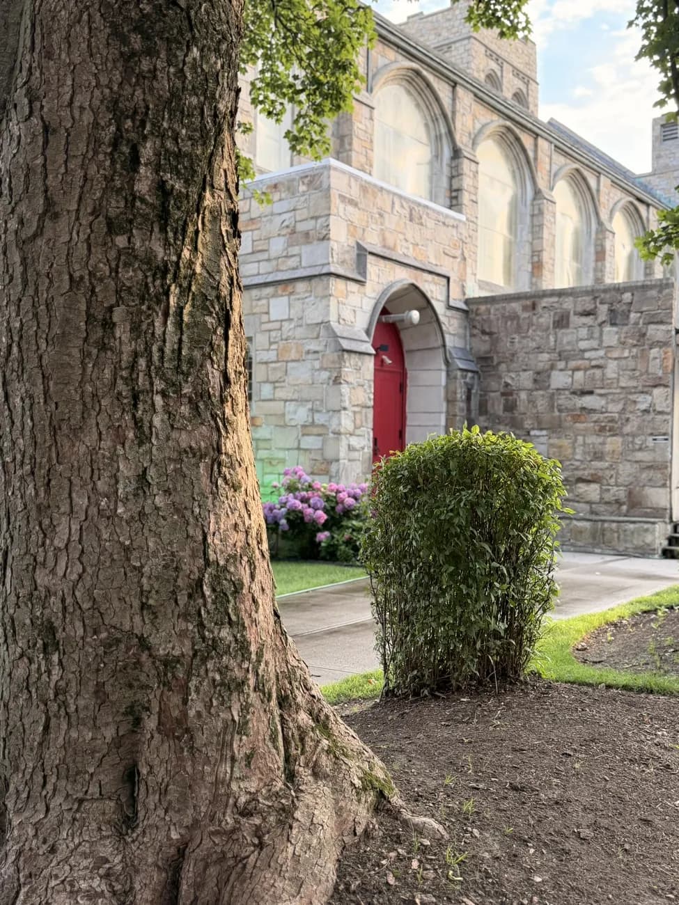 A stone church with deep red doors, set back behind old trees.