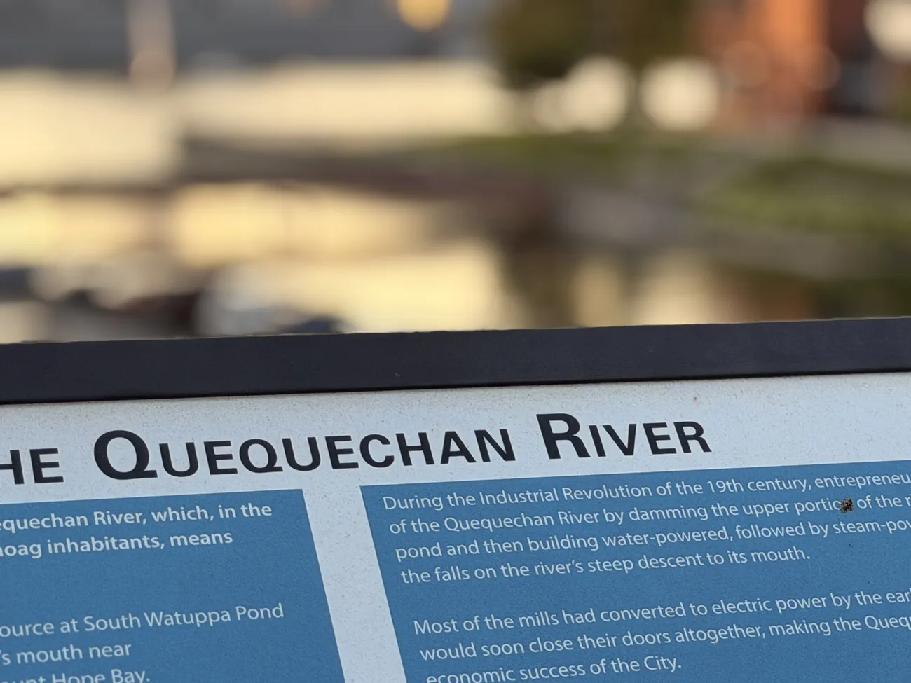 The Quequechan River interpretive sign, with the battleship beyond it.