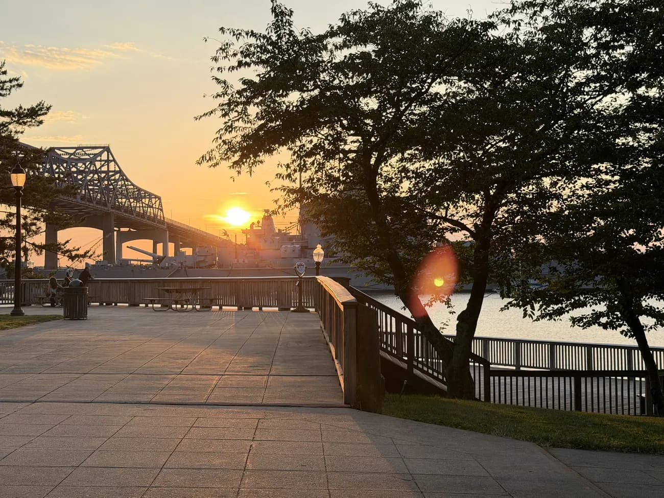 The waterfront boardwalk at golden hour, lamps coming on along the rail.