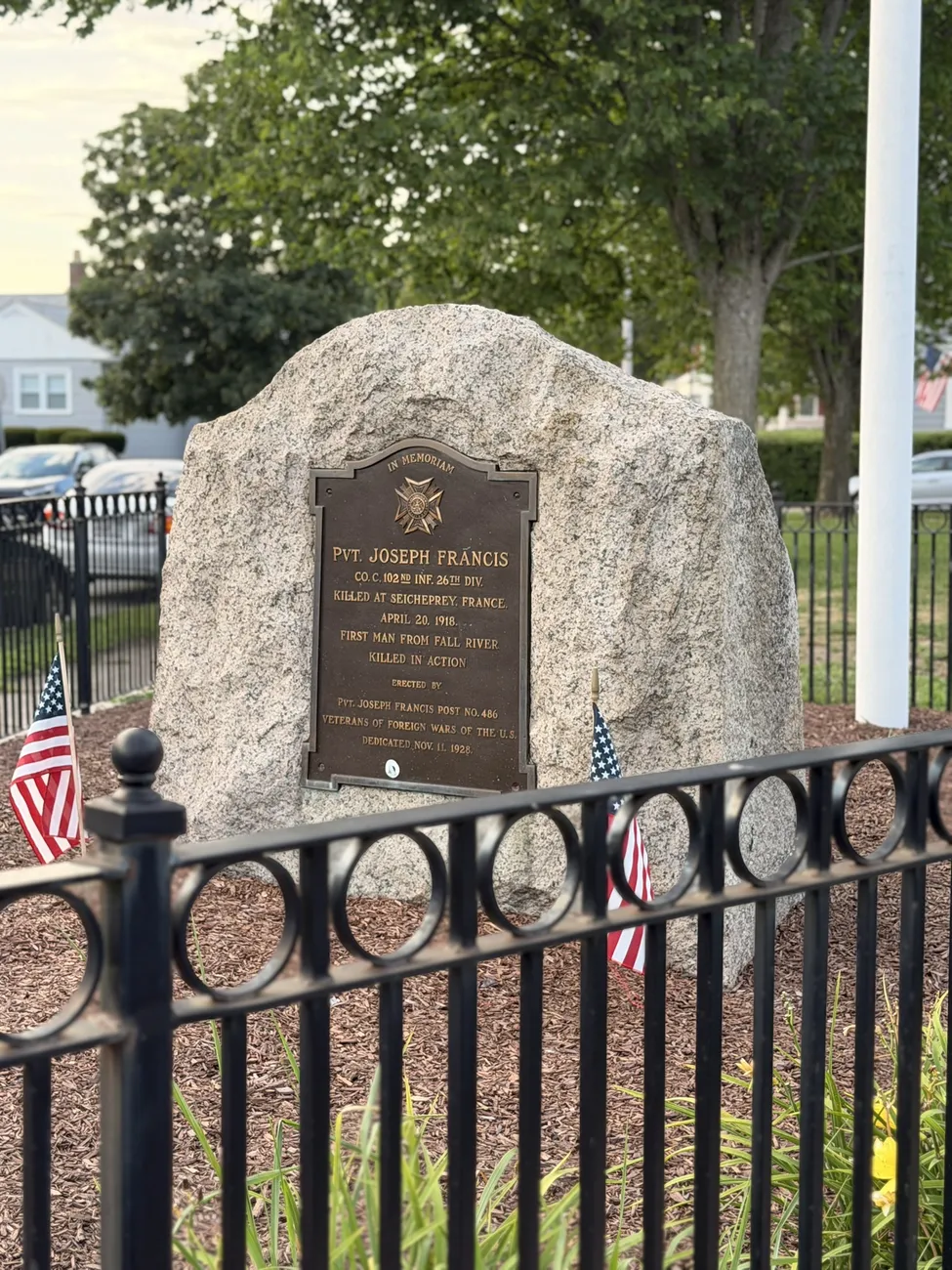 A granite memorial stone with a bronze plaque, flanked by small American flags.