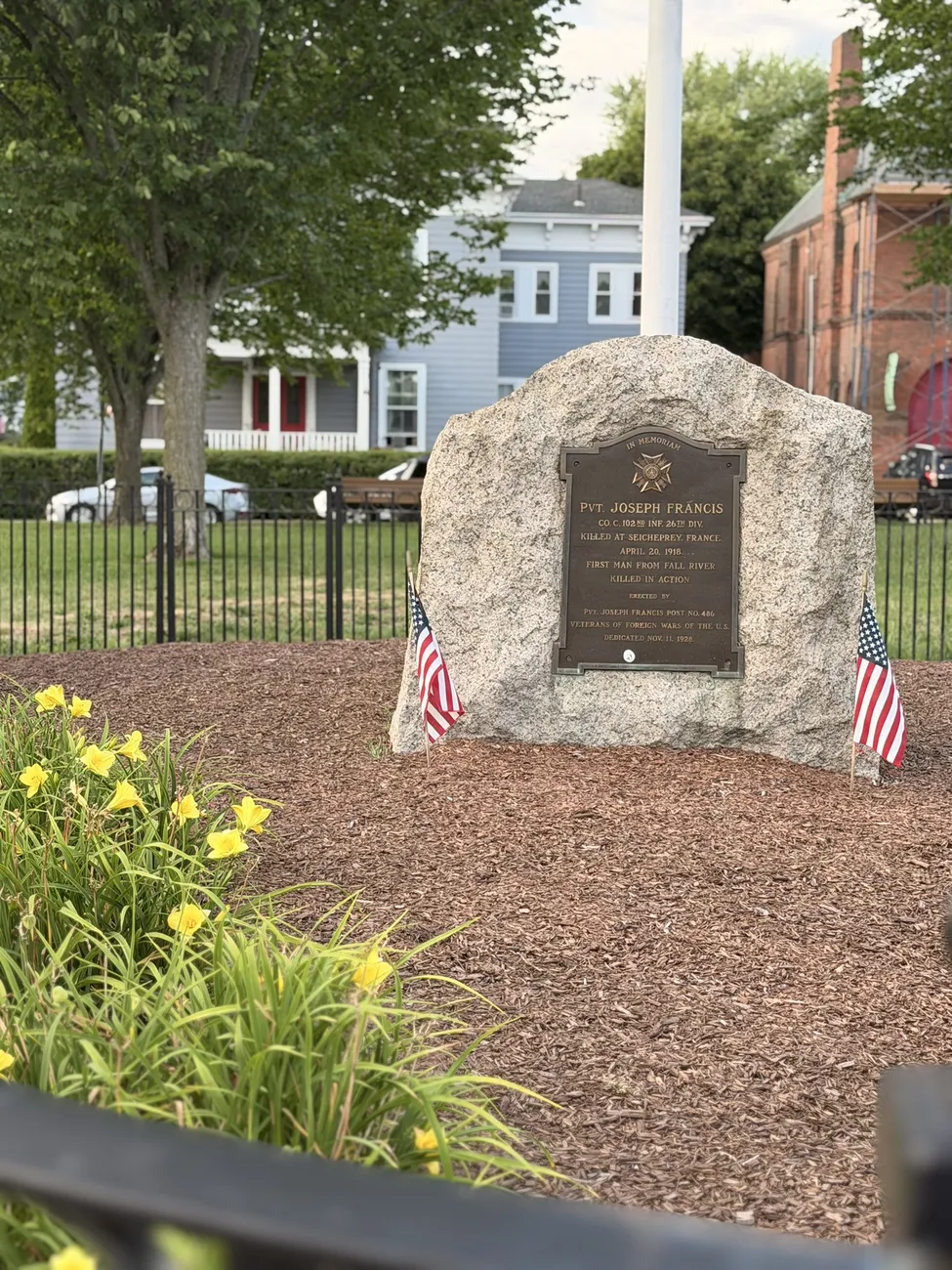 A granite memorial stone with a bronze plaque, flanked by small American flags.
