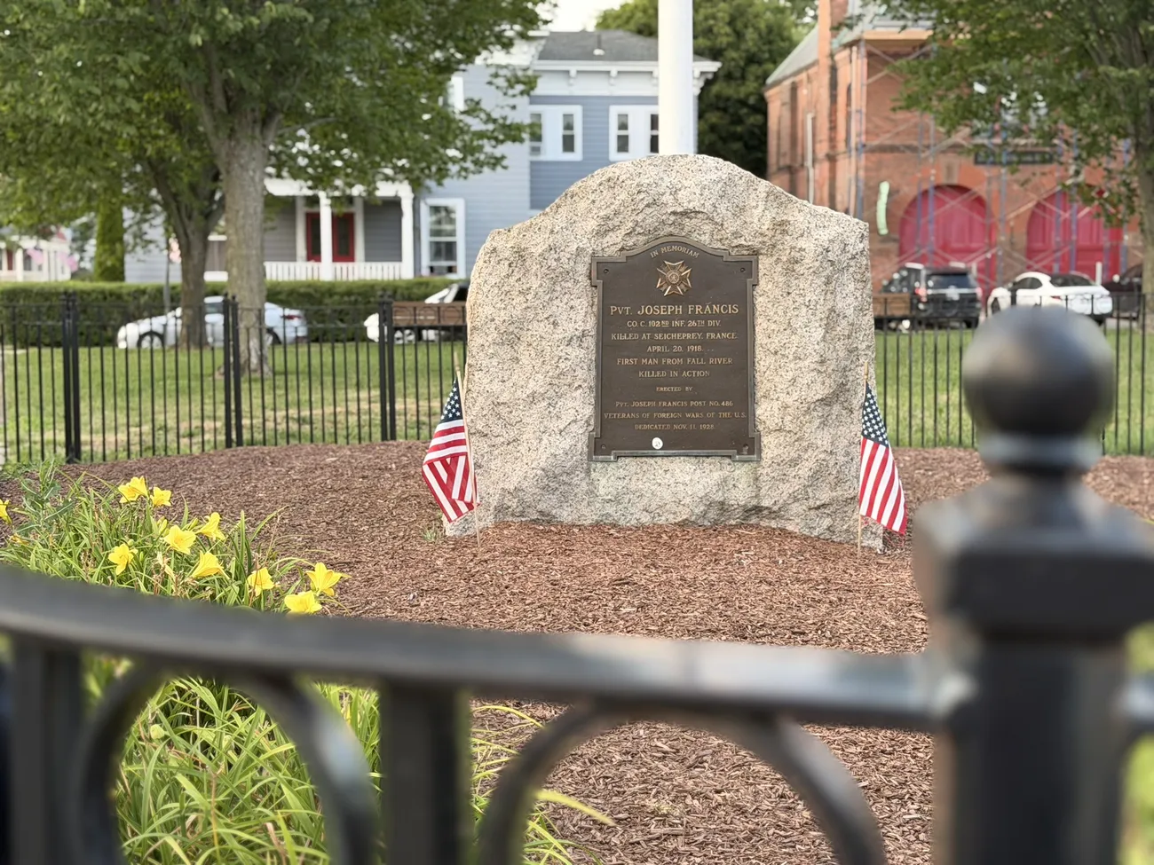 A granite memorial stone with a bronze plaque, flanked by small American flags.