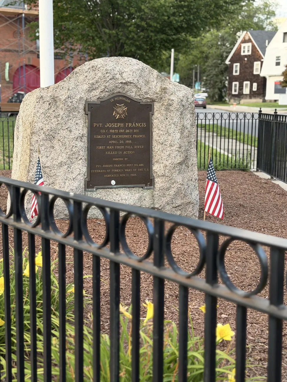 A granite memorial stone with a bronze plaque, flanked by small American flags.