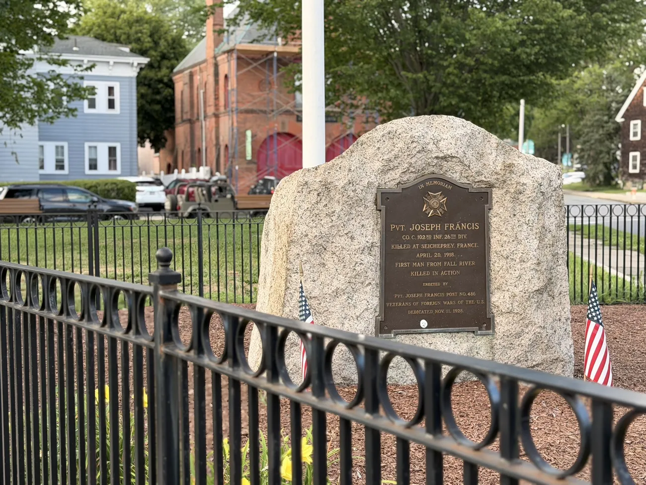 A granite memorial stone with a bronze plaque, flanked by small American flags.