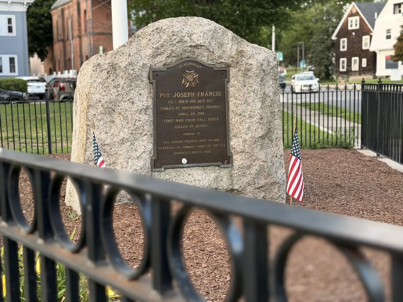 A granite memorial stone with a bronze plaque, flanked by small American flags.