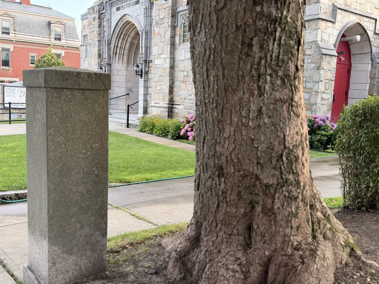 A stone church with deep red doors, set back behind old trees.