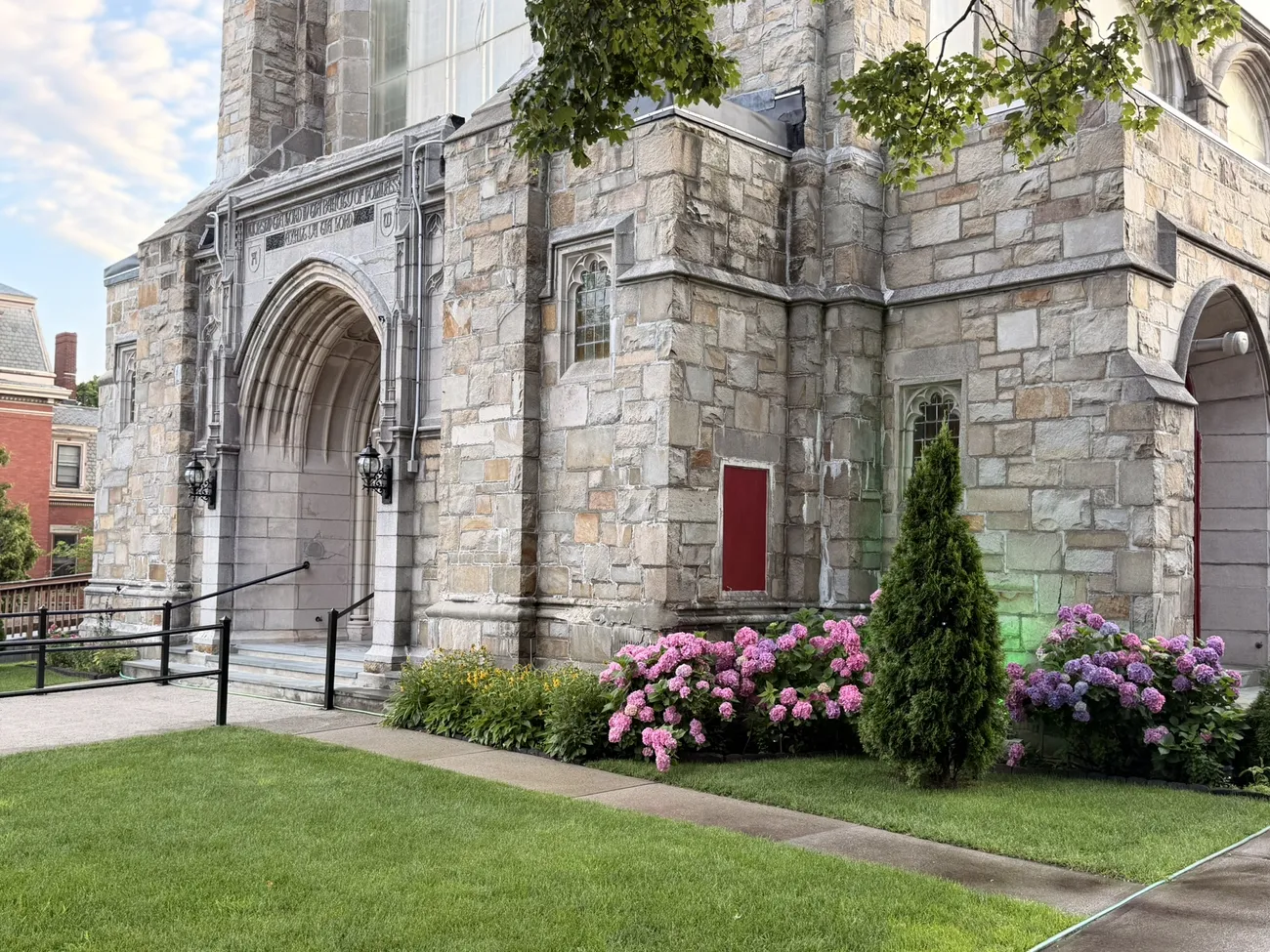 A stone church with deep red doors, set back behind old trees.