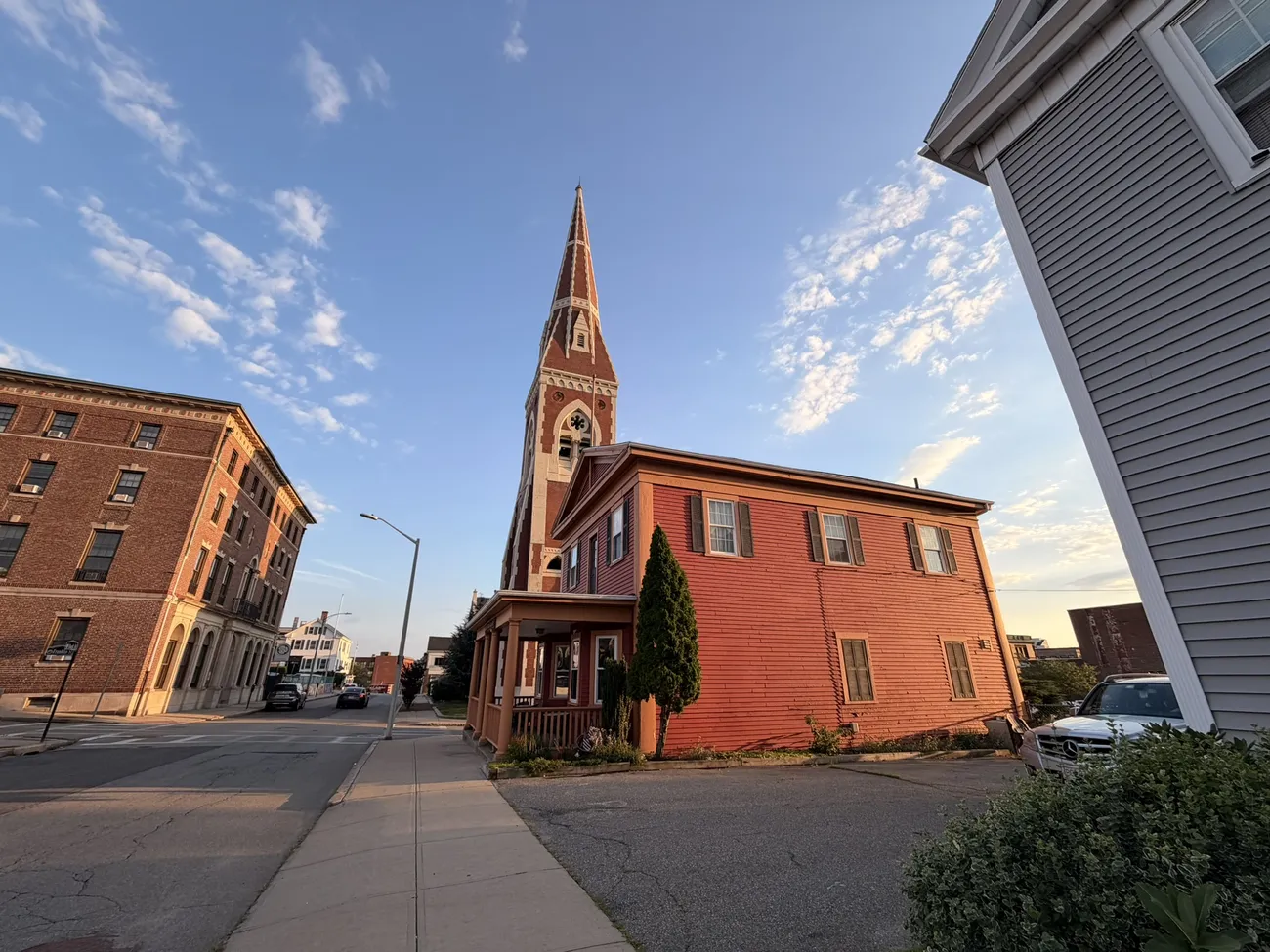A church spire and red clapboard building at golden hour on a downtown Fall River street corner