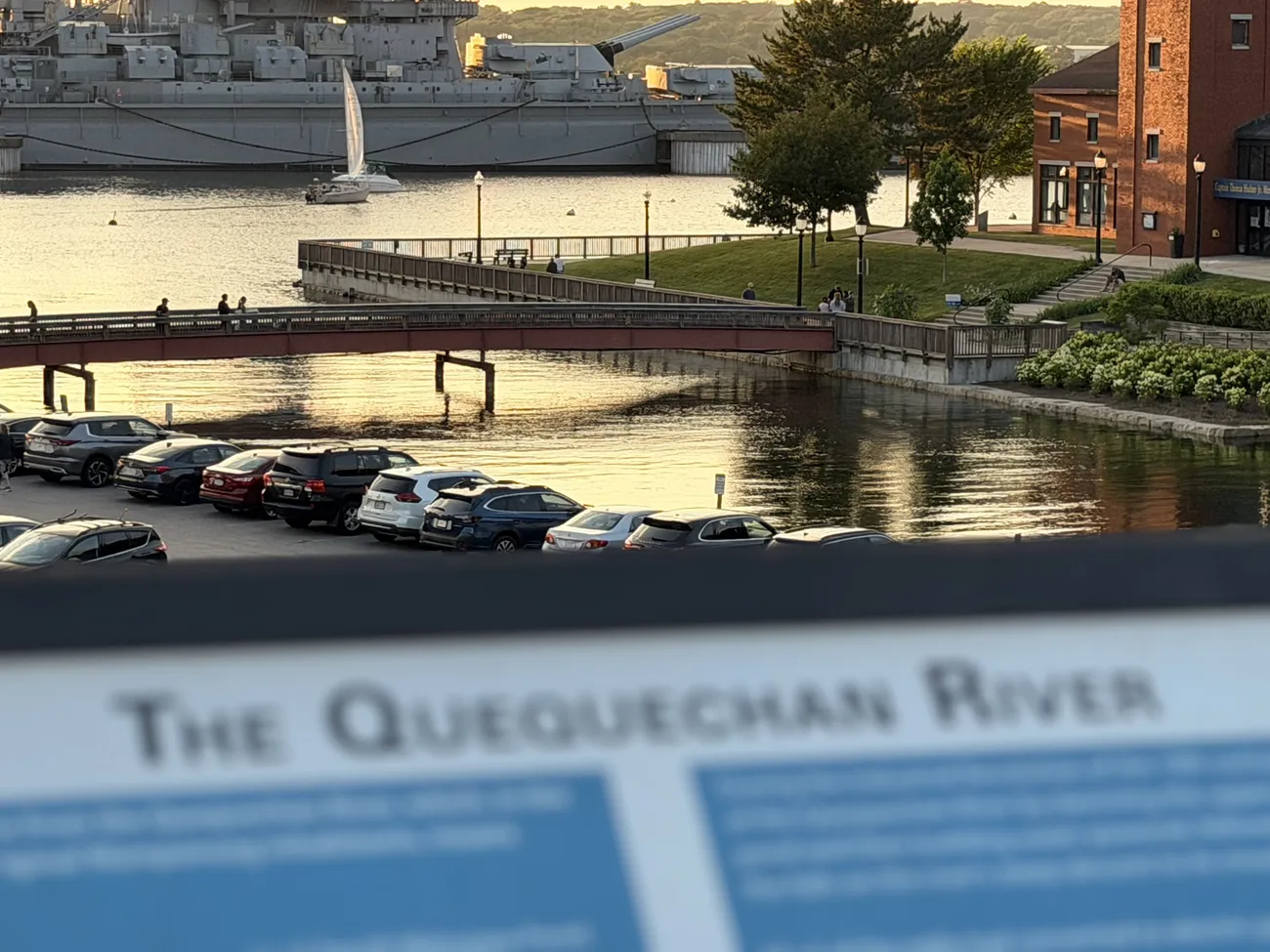 The Quequechan River interpretive sign, with the battleship beyond it.