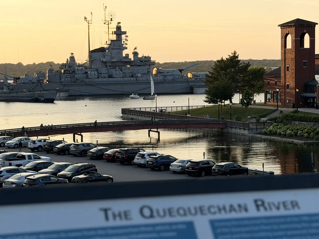 The Quequechan River interpretive sign, with the battleship beyond it.