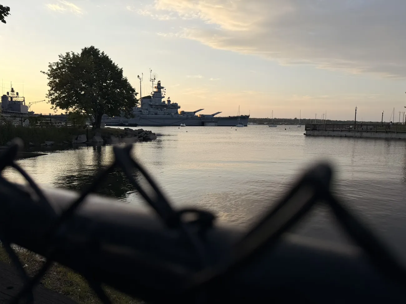 The battleship at Battleship Cove, seen through a chain-link fence at dawn.