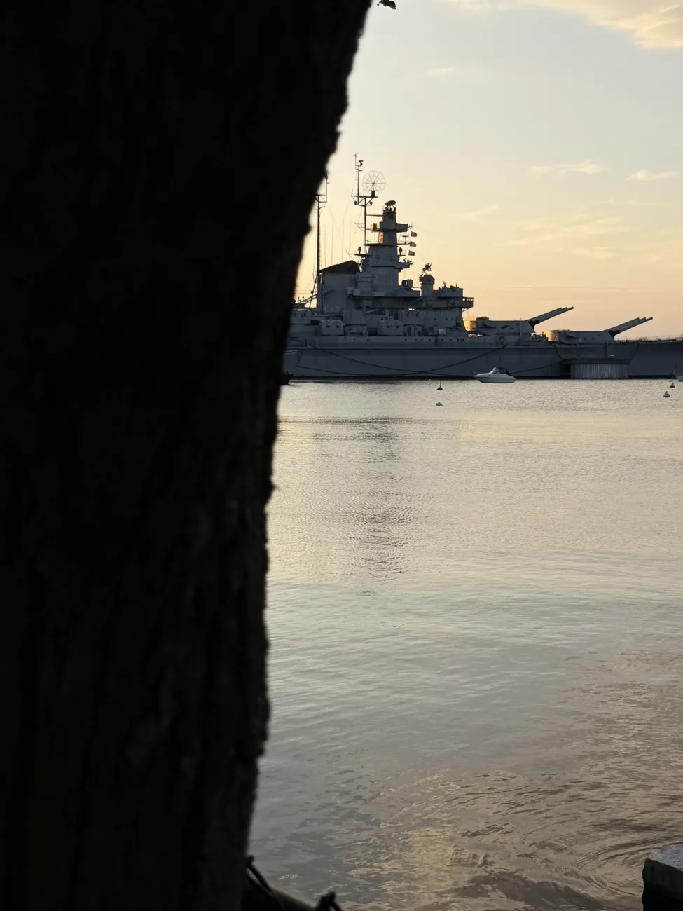 The battleship at Battleship Cove, seen through a chain-link fence at dawn.