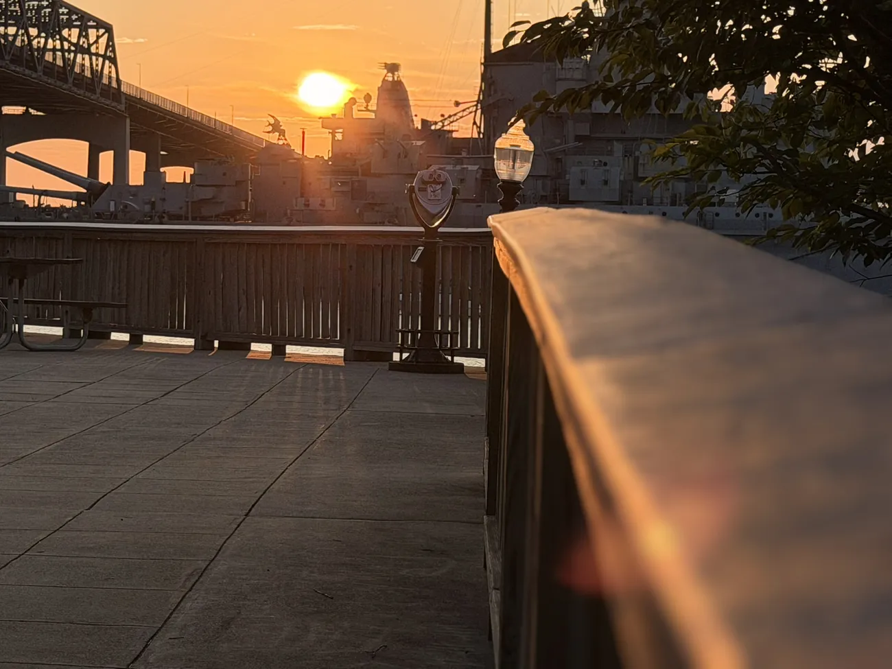 The waterfront boardwalk at golden hour, lamps coming on along the rail.