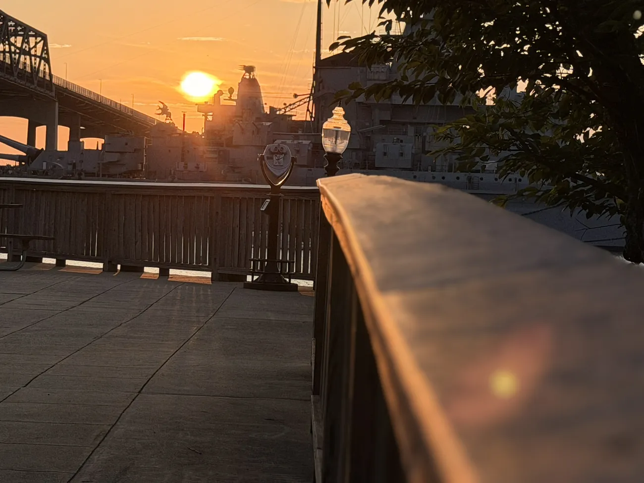The waterfront boardwalk at golden hour, lamps coming on along the rail.