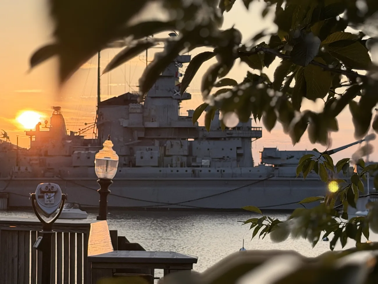 The waterfront boardwalk at golden hour, lamps coming on along the rail.